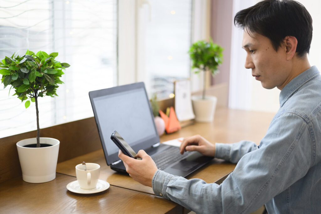 A man working on his laptop and phone to set up a Malaysia online payment gateway.