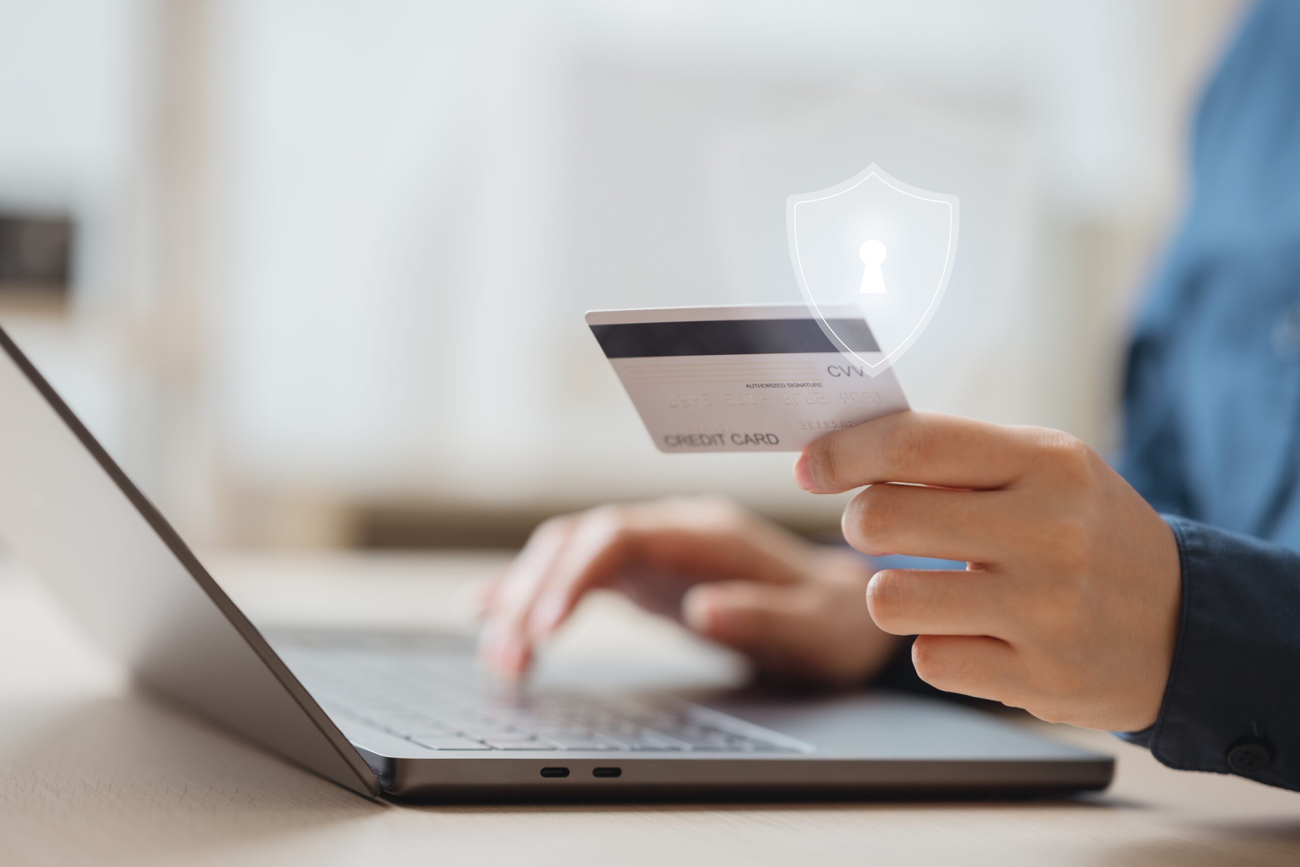  Person holding credit card at laptop with security shield for protected online card payment 